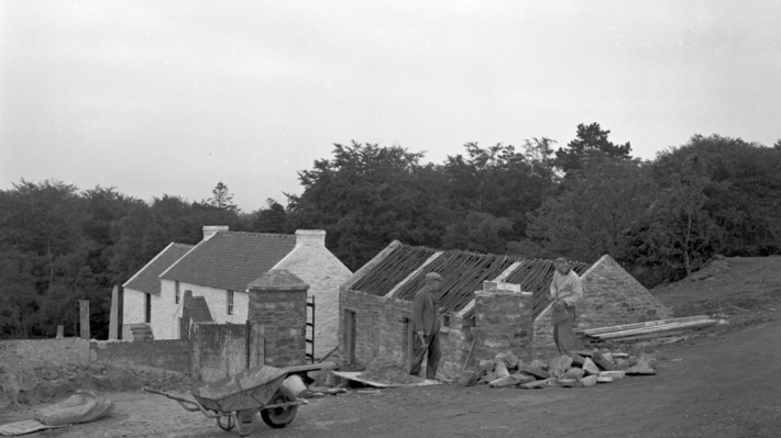 a black and white image of buildings at the ulster folk museum and two men building a wall 