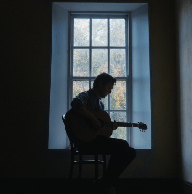 Joshua Burnside silhouetted by the window with his guitar