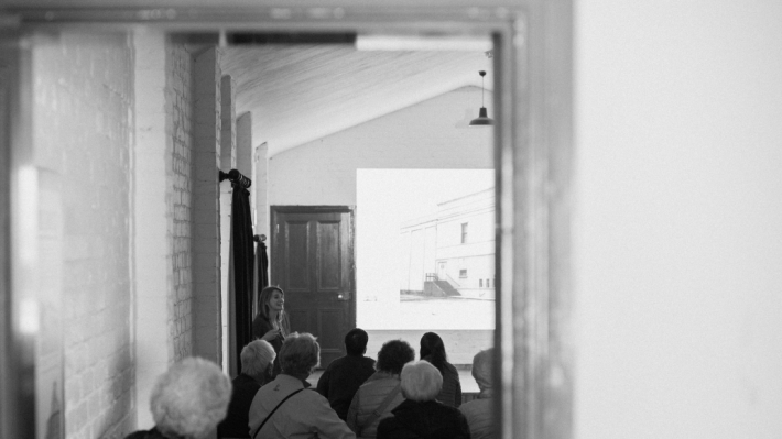 A black and white image of backs of heads and a lady giving a lecture