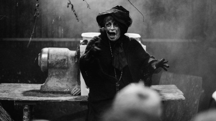 A black and white image of a lady dressed up as a witch, speaking into a mic headset