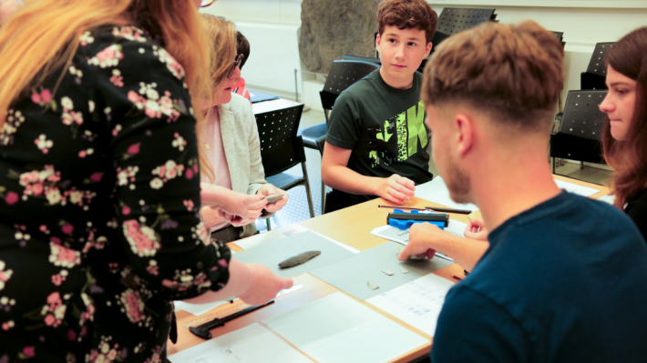 A group of young people sit at a table with archaeological objects.