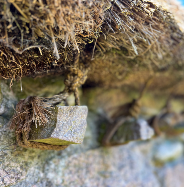 A close-up of a stone jamb in an outer cottage wall with thatch rope tied to it. 