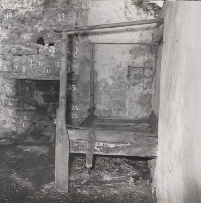 The inside of a run-down cottage. The stones of the walls are numbered with white chalk.