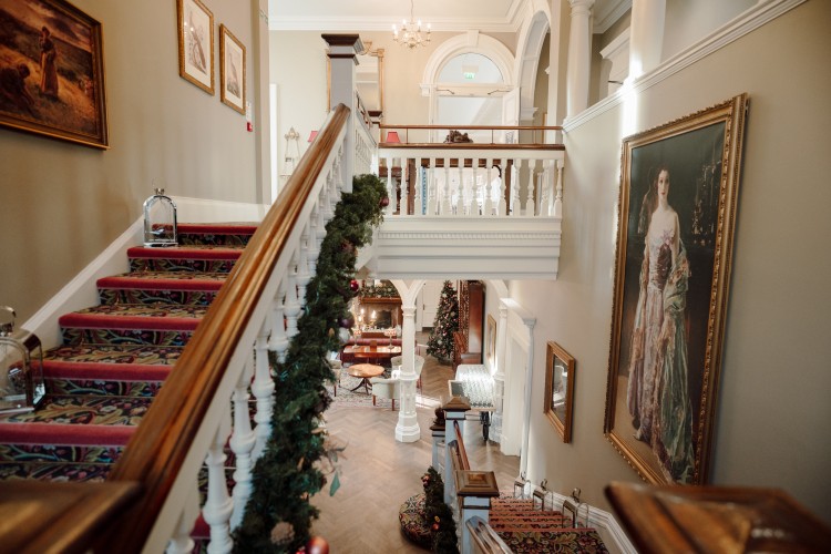 A Christmas garland added to the staircase in Cultra Manor. Grand, portrait paintings hang on the walls.