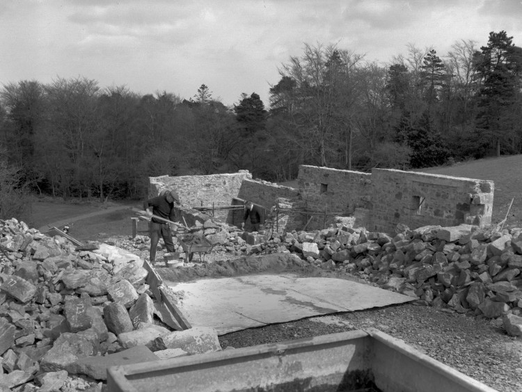 A man stands in the middle of a house being built. The nearby stones are numbered.