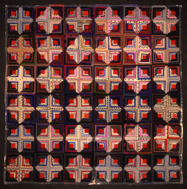 A dark-coloured patterned quilt, with lots of cross, diamond and square patterns.