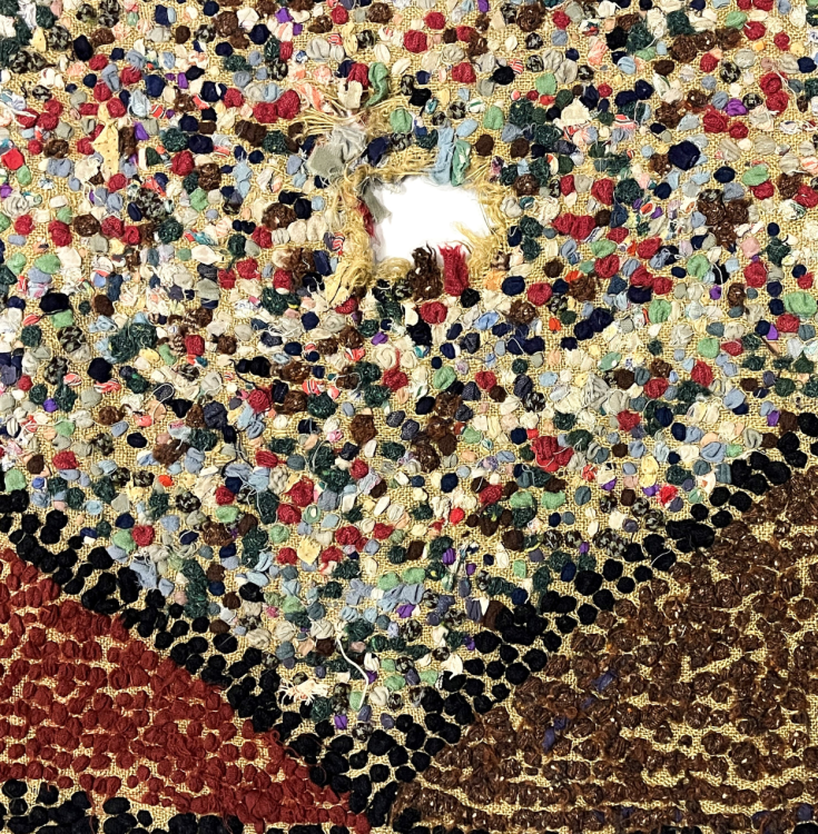 A detail shot of a rug. We can see a multicolour section with a hole. The outer sections are brown and red..