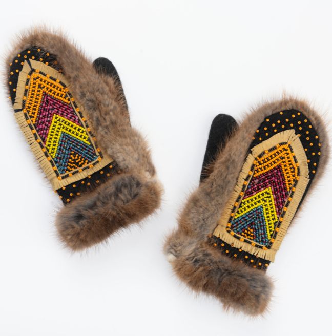 A pair of fur gloves with beading on the back of the hands. The beads are in a v shape pattern and layered by colour, from bottom to top: green, yellow, red, and orange.