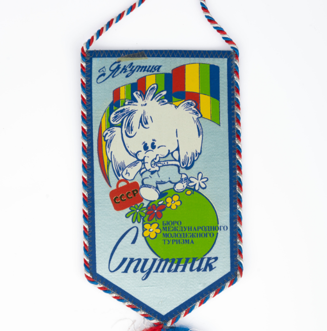 A small banner. The edges are in rainbow thread. The banner is light blue with images and cyrillic text. The image is a cartoon elephant on a green globe with flowers, holding a red briefcase with USSR written on it, and a rainbow background.