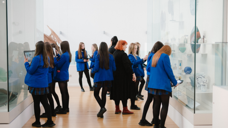 A classroom of girls wearing blue uniforms looking at the glass-fronted displays in the Applied Art Gallery of the Ulster Museum.