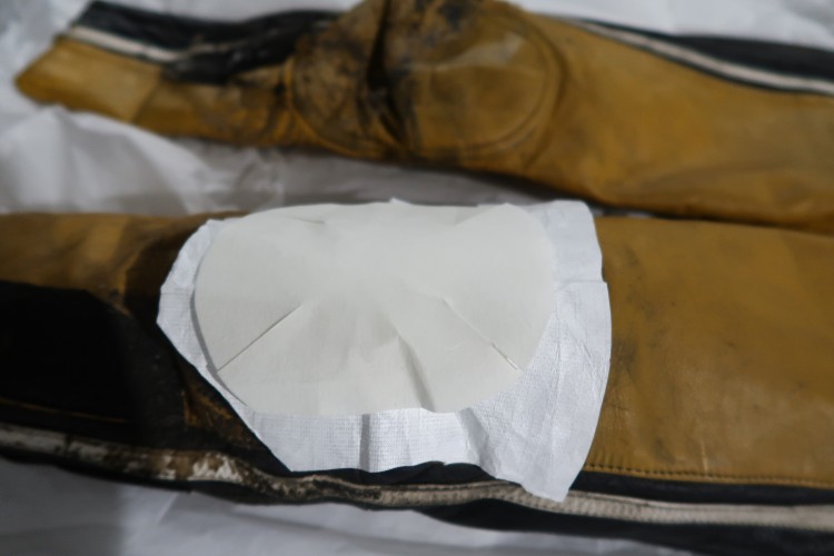 A close up of the knee of a yellow and black jumpsuit with a piece of white cloth over it. Over the cloth is a smaller piece of white cloth.