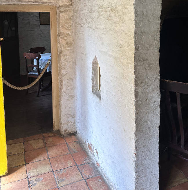 An interior jamb wall; a white stone wall with a little window sits between the front door and the rest of the room.