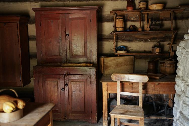 A view inside a log cabin, with a table and sideboard on the left, and a chair and fireplace to the right.