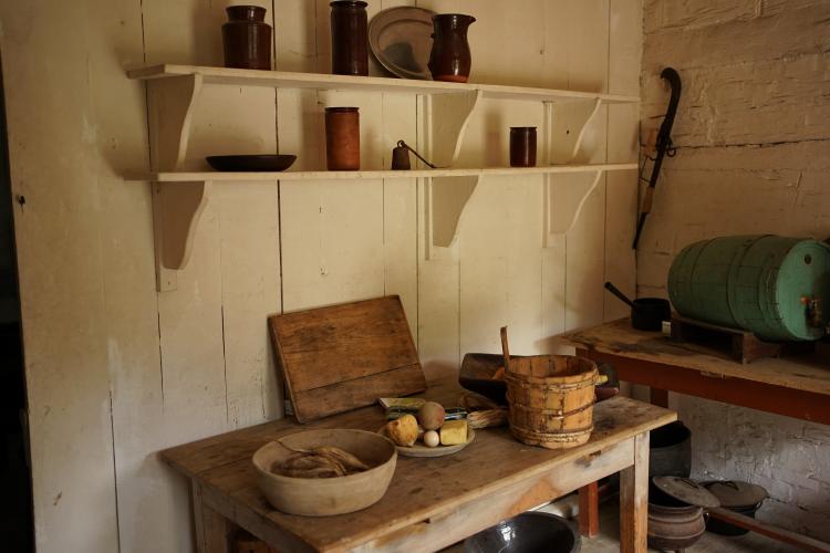 The kitchen of a log farmhouse, showing shelves and a side table.