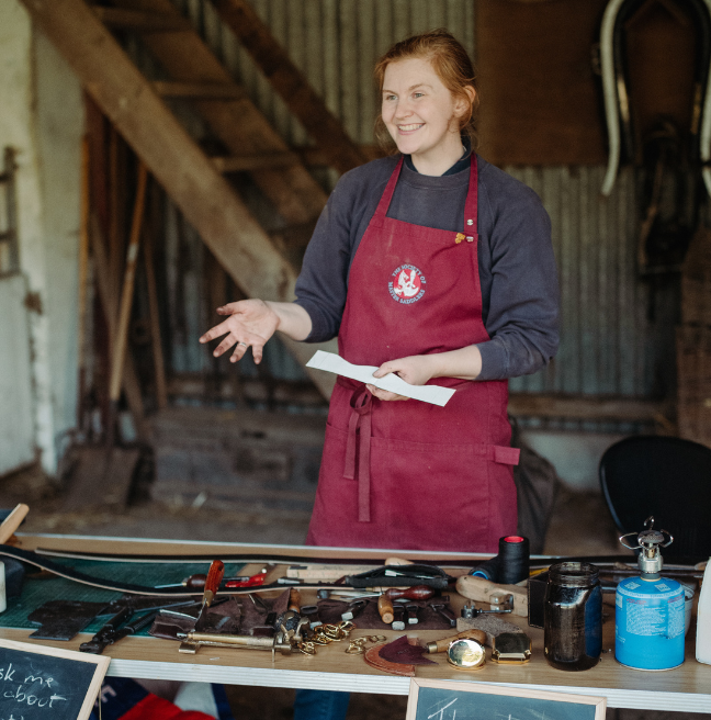 a red haired woman working with leather in a red apron 