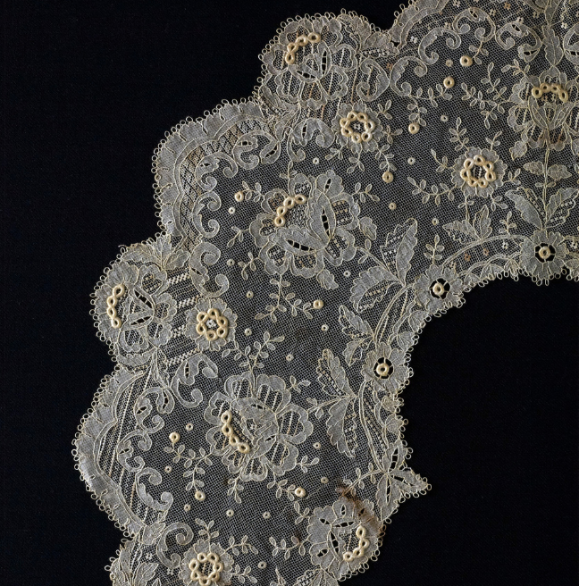A close up of an intricate lace collar wtih many small floral designs.