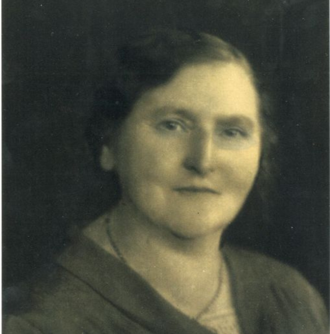 A black and white photograph portrati of a woman. She is turned towards the camera with a slight smile.