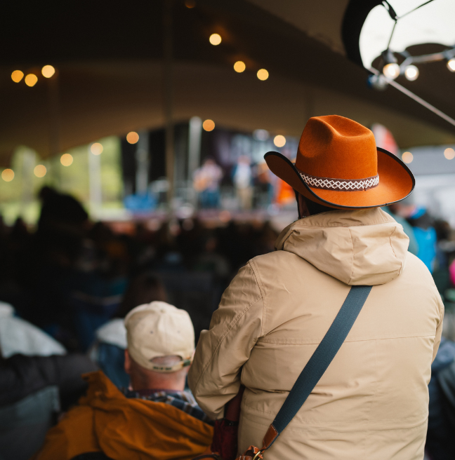 A person in an orange cowboy hat watching music 