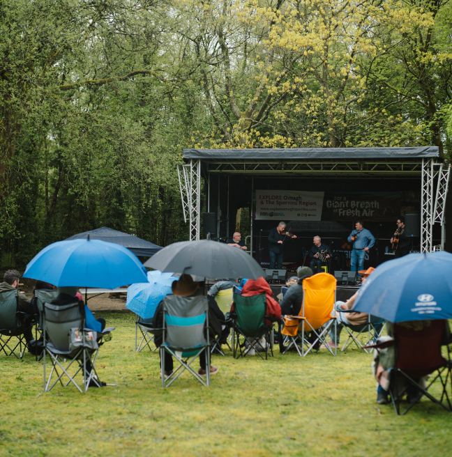 A crowd of people watching a stage in the rain with umbrellas up 