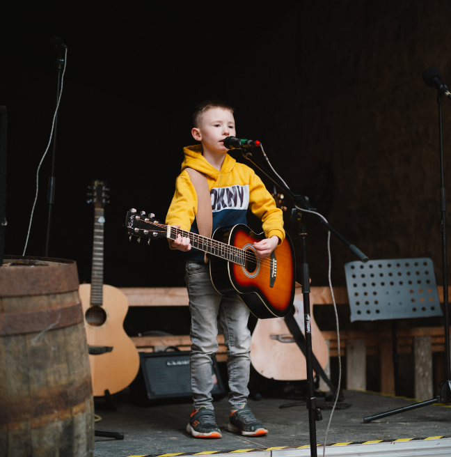 A child in a yellow jumper dinging at an open mic 