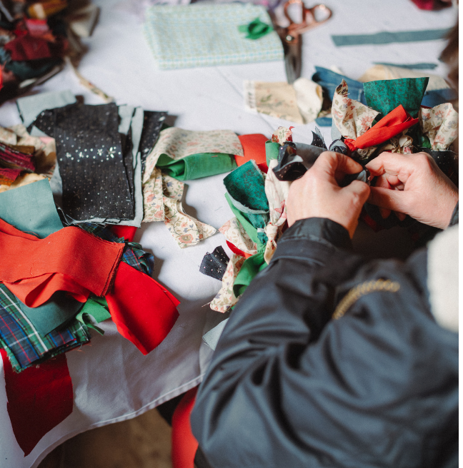hands creating a red and green rag wreath