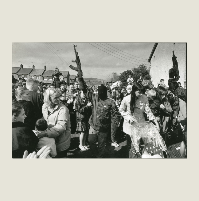 Black and white photograph of a crowd with men in balaclavas holding rifles