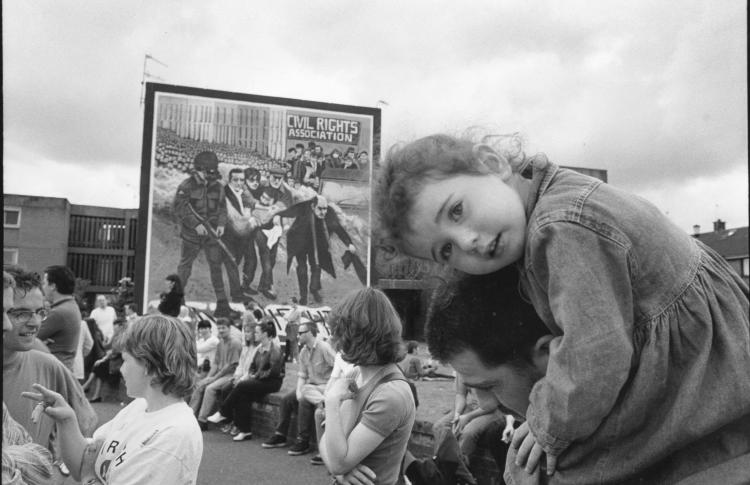 Black and white photograph of Bloody Sunday rally, young child on adults shoulders looking at the camera in the foreground