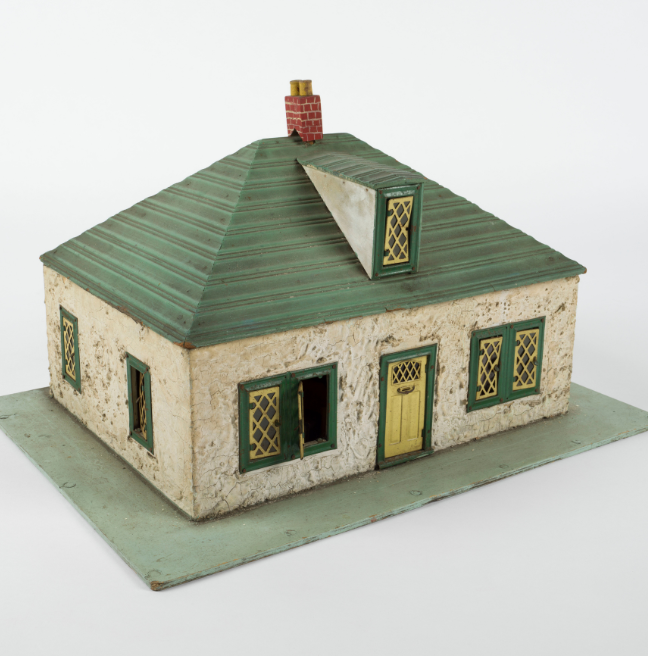 A small square dolls' house with a green roof, a yellow door, and a green base for a small garden.