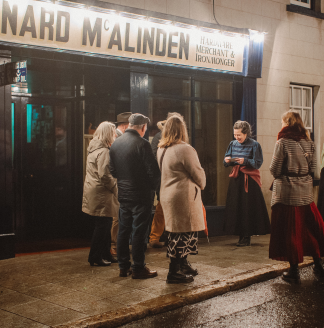 a group of adults standing outside an exhibit building at ulster folk museum