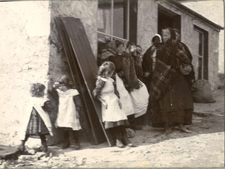 A woman and children stand outside their cottage wearing traditional dress in the early 1900s.