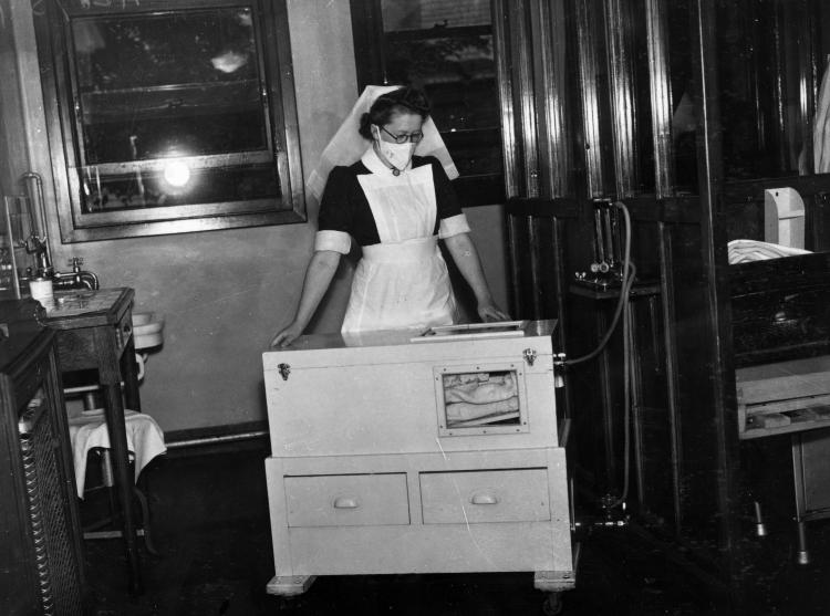 A nurse stands over an electrically-heated cot.