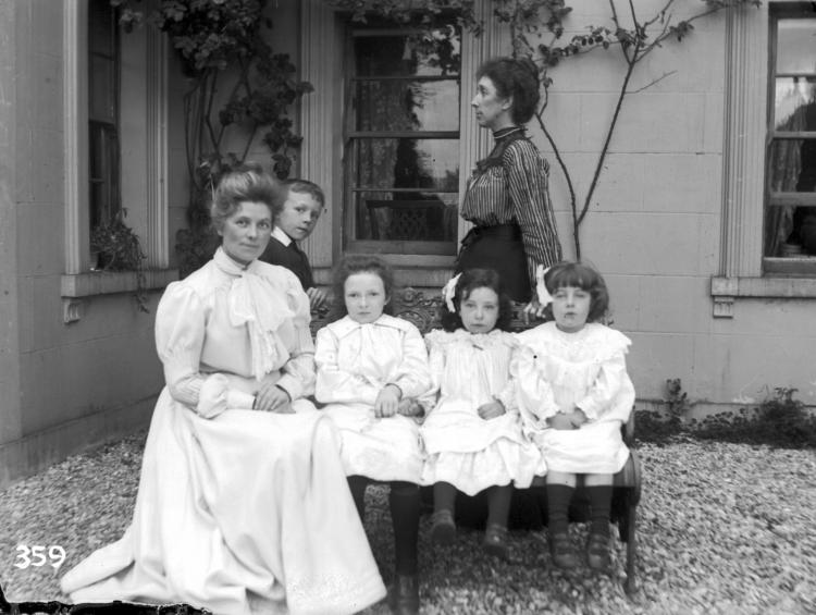 Two women sit with three children looking very well to do in the early 1900s. 