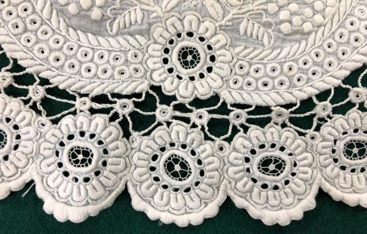 Detail of white embroidery on a dress collar from c.1860. It's placed on a black background which is showing through the embroidery detail.