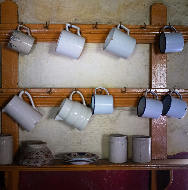 A mug rack with nine mugs hanging on its frame.