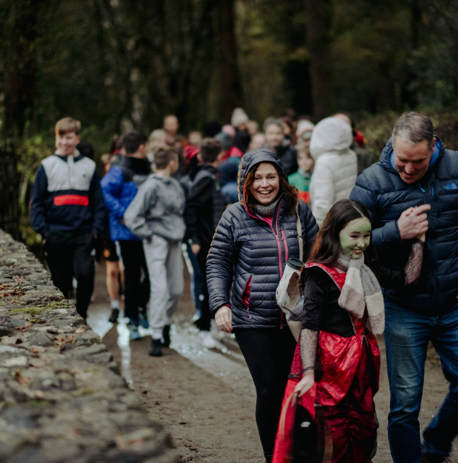 A group of adults and children in halloween dress crossing a bridge