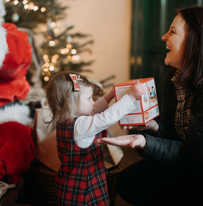 A little girl handing her  mum a present and the mum is laughing 