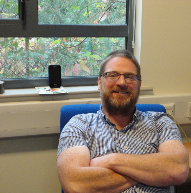 A man sits smiling with crossed arms in his office.