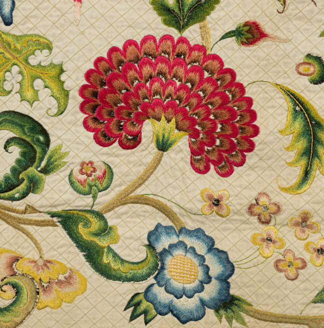 A detailed image of the embroidery on the Lennox Quilt, showing a bright red flower, a quaint blue flower, and lots of leaves and small flowers dotted around.