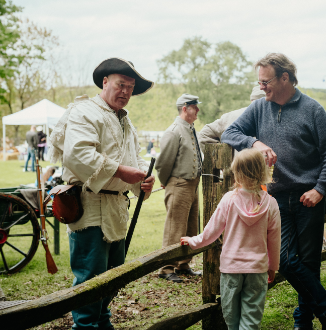 An actor dressed in costume like he's in the American War of Independence, talking to visitors over a fence.
