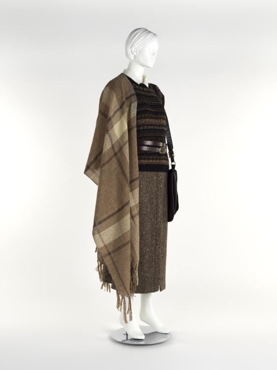 A mannequin with a long tweed skirt, a shirt and sweater vest with a belt at the waist, and a long caramel tartan scarf draped over the shoulder.