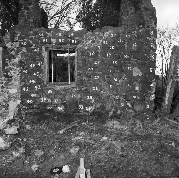 A black and white photograph of a dilapitated house, with chalk numbers on its bricks.