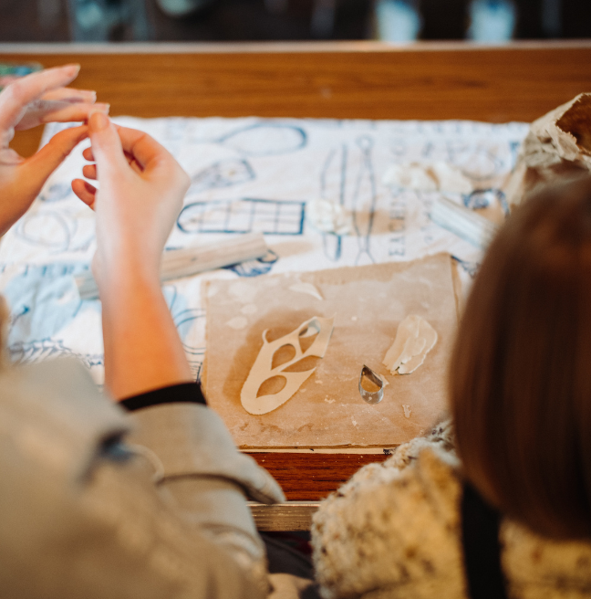 a womans hands doing crafts and a child sitting next to her