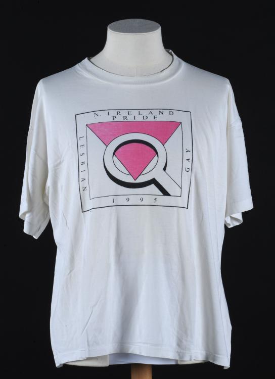 A white tshirt made for the fifth pride in Belfast. The logo has a pink inverted triangle and a magnifying glass.