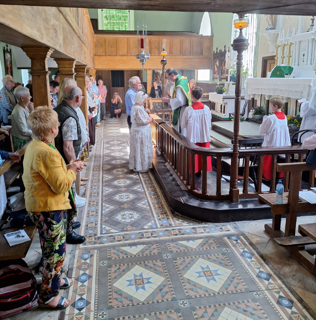 Two people stand at the altar of a Catholic Church. A Priest is praying.