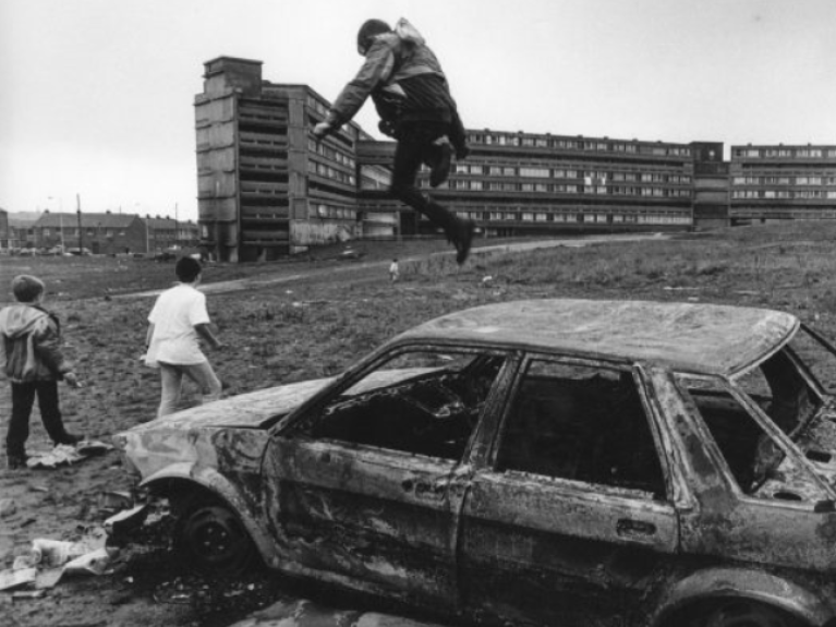 Children jumping on top of a burnt out car