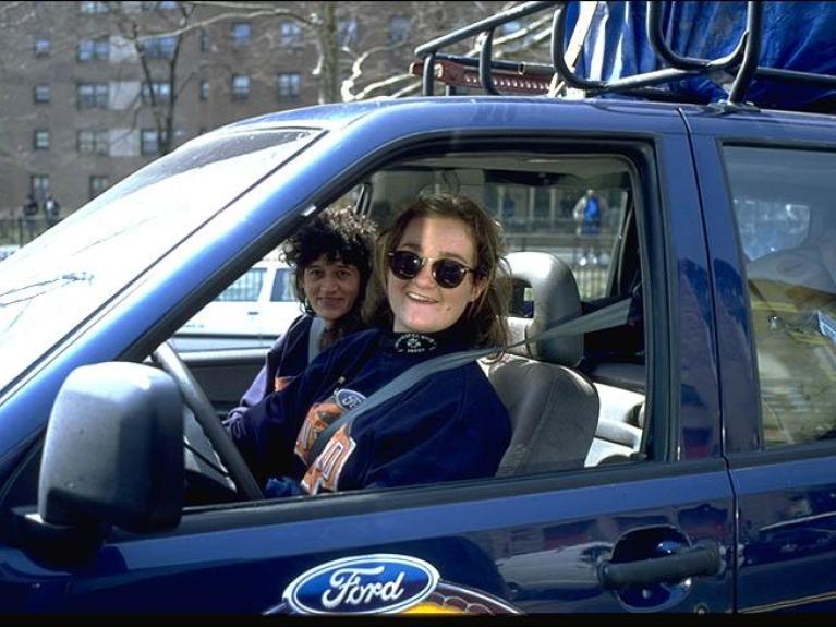 A woman smiles out the window of a blue Ford car.