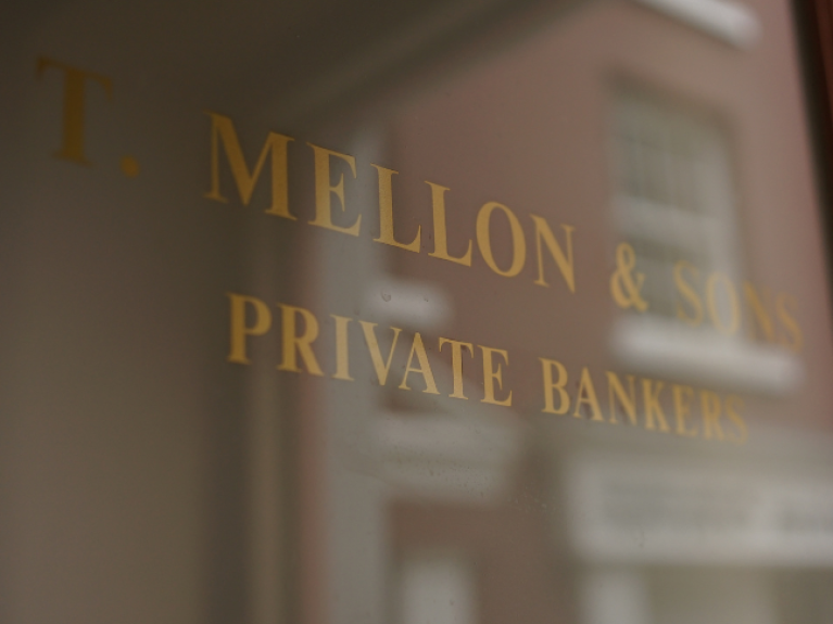 The glass door to a bank, etched with the words 'T Mellon & Sons, Private Bankers'