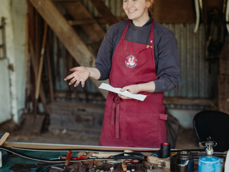 a red haired woman working with leather in a red apron 