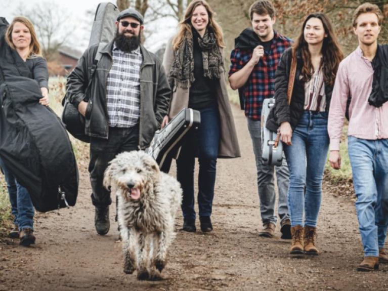 a six piece band with men and woman carrying instruments and a white dog (band named King Springs Road)