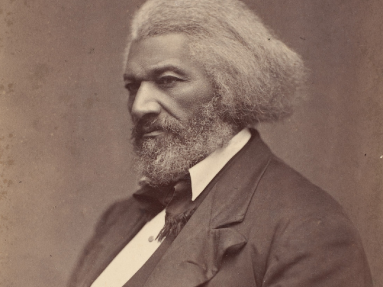 A man sits for a photograph in the late 1800s. He looks strong and stoic, facing away from the camera. 